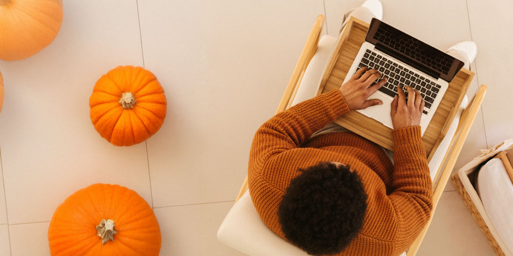 Person using a laptop on a stool with pumpkins around